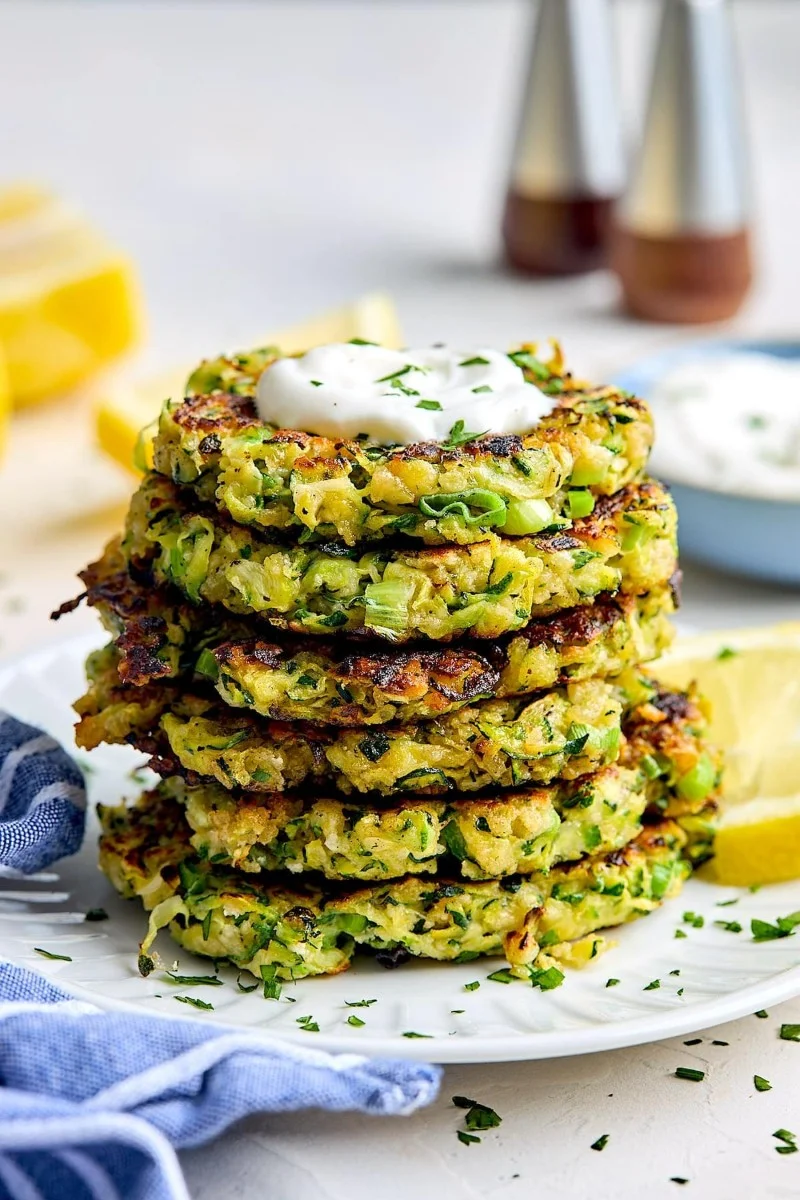Crispy zucchini fritters on a plate garnished with herbs and a dipping sauce